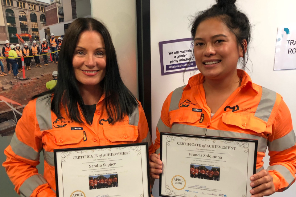 Women in Construction - image of two female graduates wearing high vis shirts and certificates of achievement