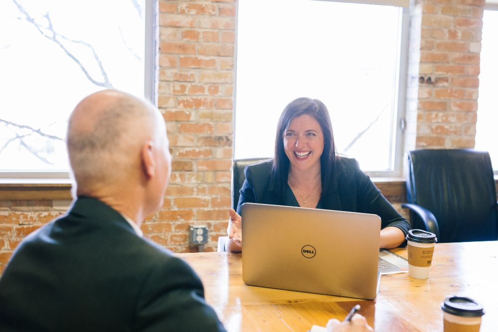 Record placement for Jobfind - image of a smiling woman sititng at a desk in front of a laptop and smiling at a bald man sitting opposite