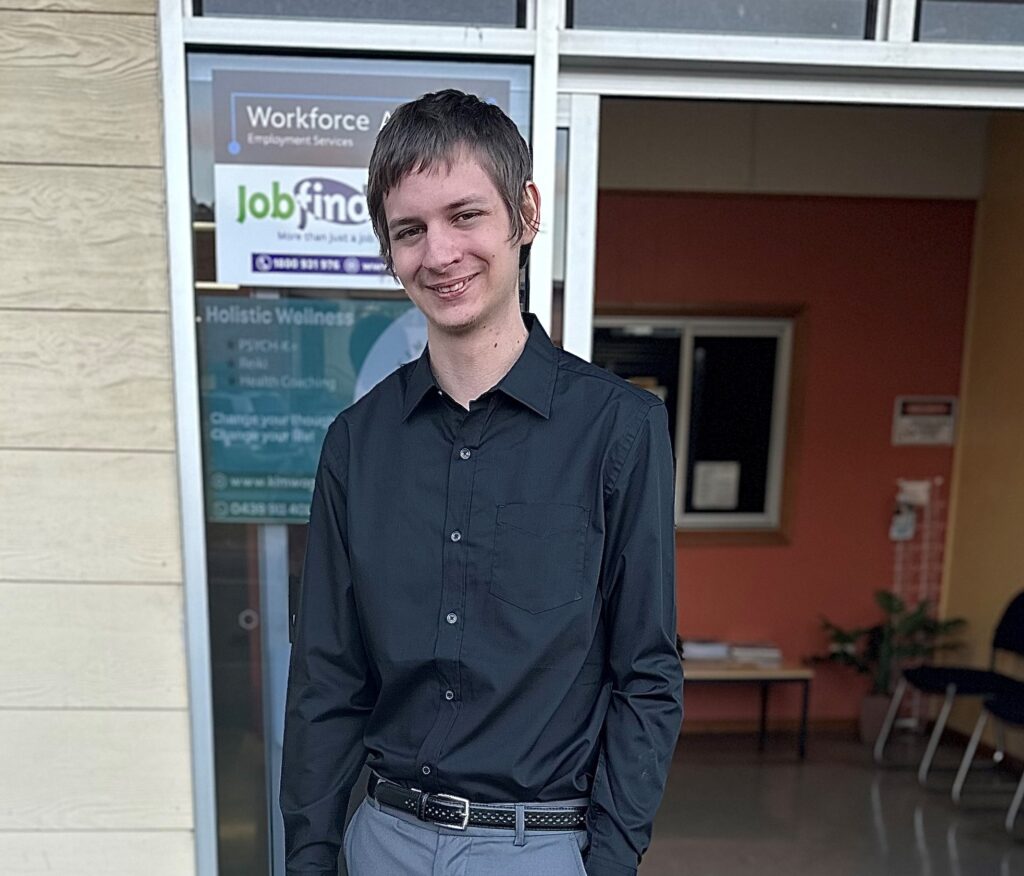 A young man in long sleeved black shirt stands in front of Jobfind office