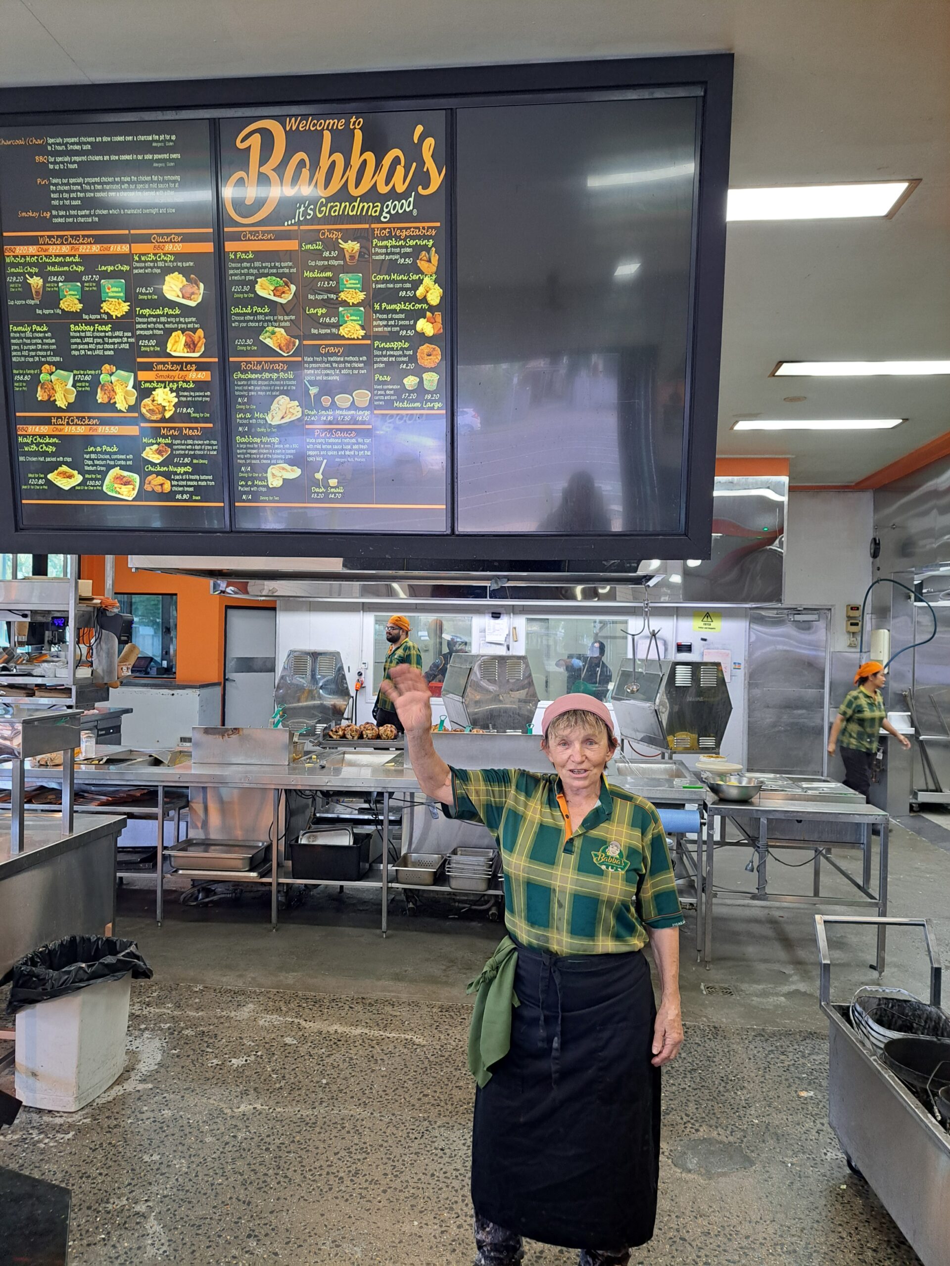 Nadia Softa smiling at the camera and pointing up at a menu on the wall above her.