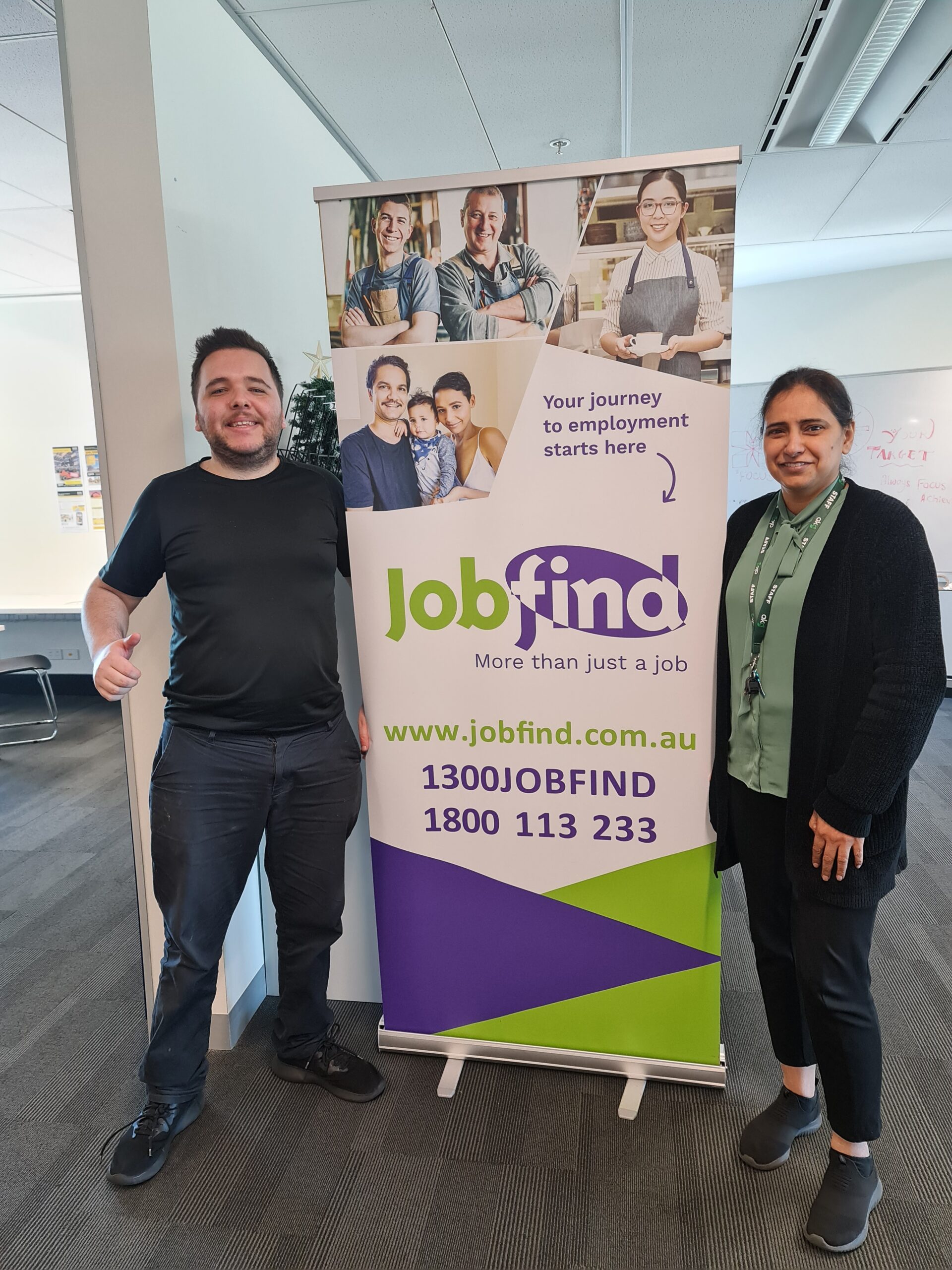 Image of Sumandeep and Alexander standing beside a Jobfind pull up banner. Both are smiling and facing the camera.